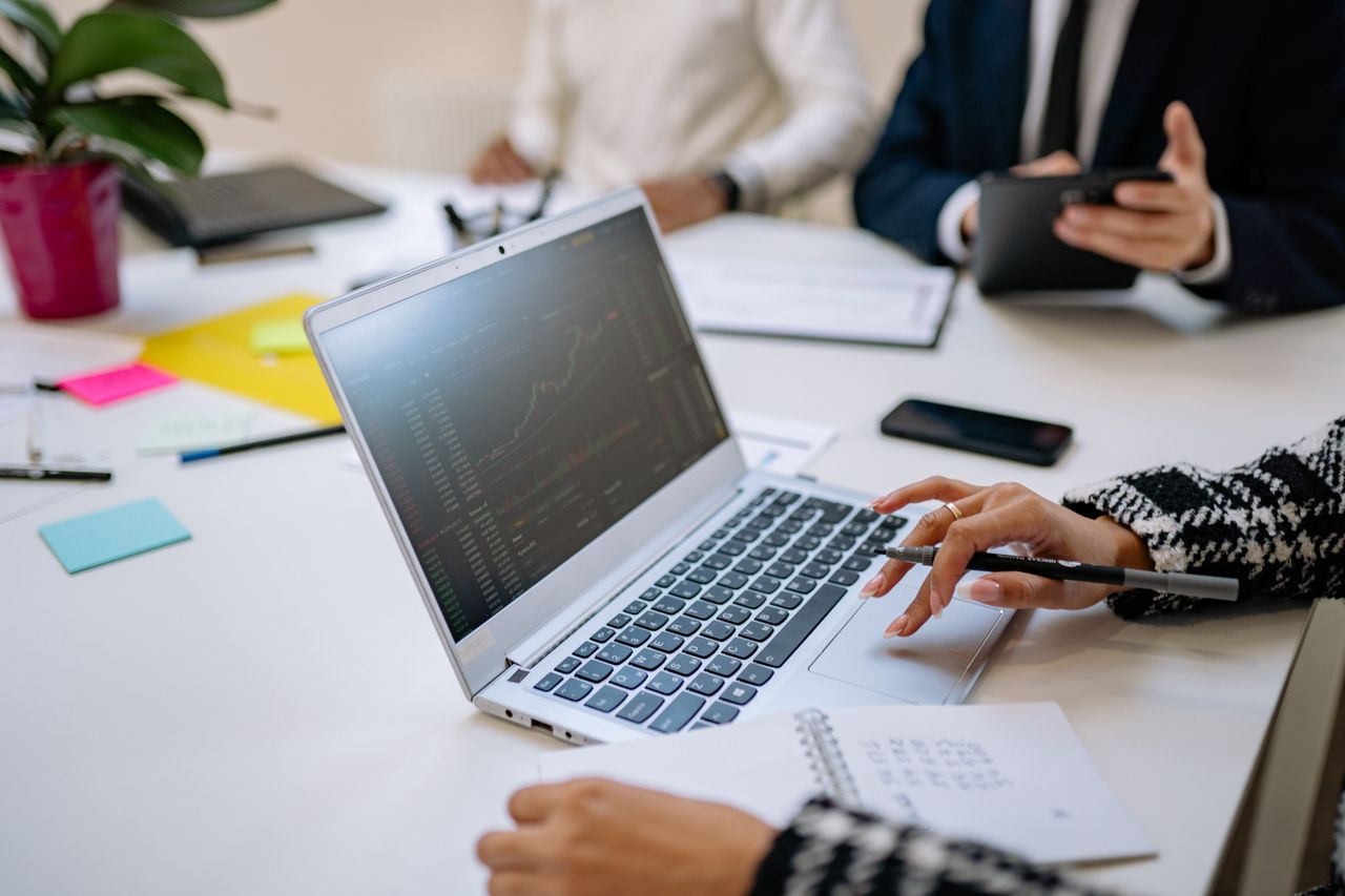 Professionals analyze financial data on laptop during office meeting.